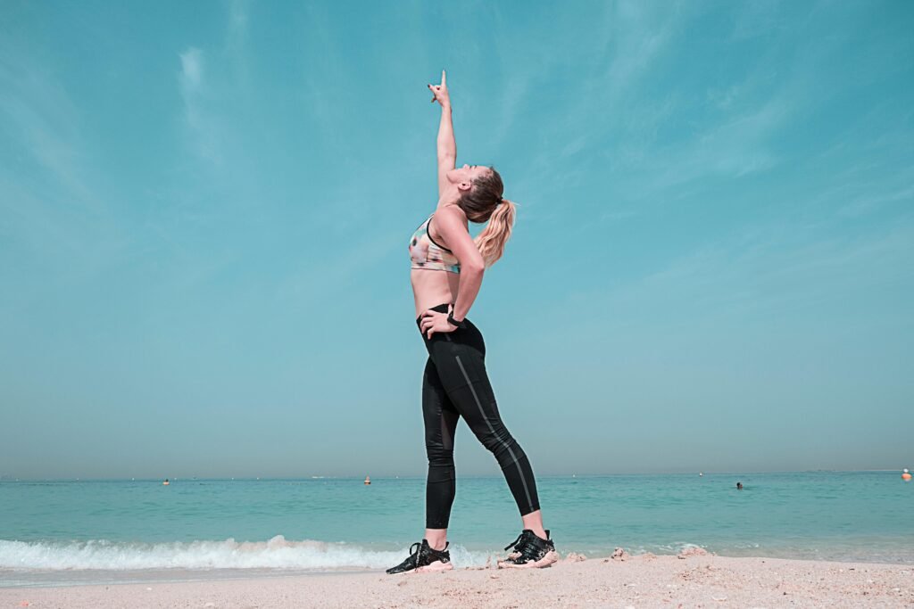 A woman performing a stretching exercise on a sunny beach in Dubai.