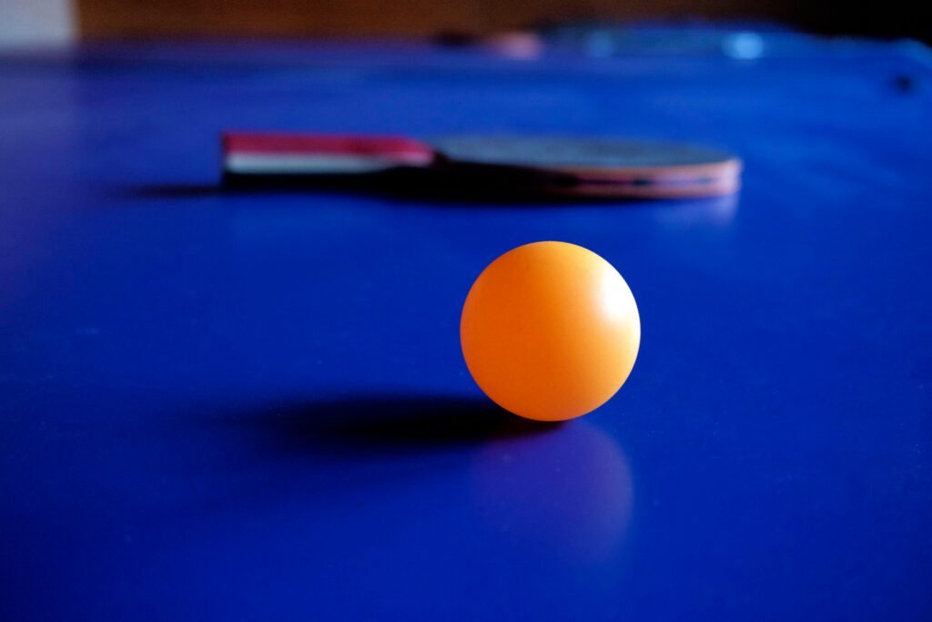 Vibrant orange ping pong ball with a table tennis racket on a blue table, emphasizing sport and leisure.