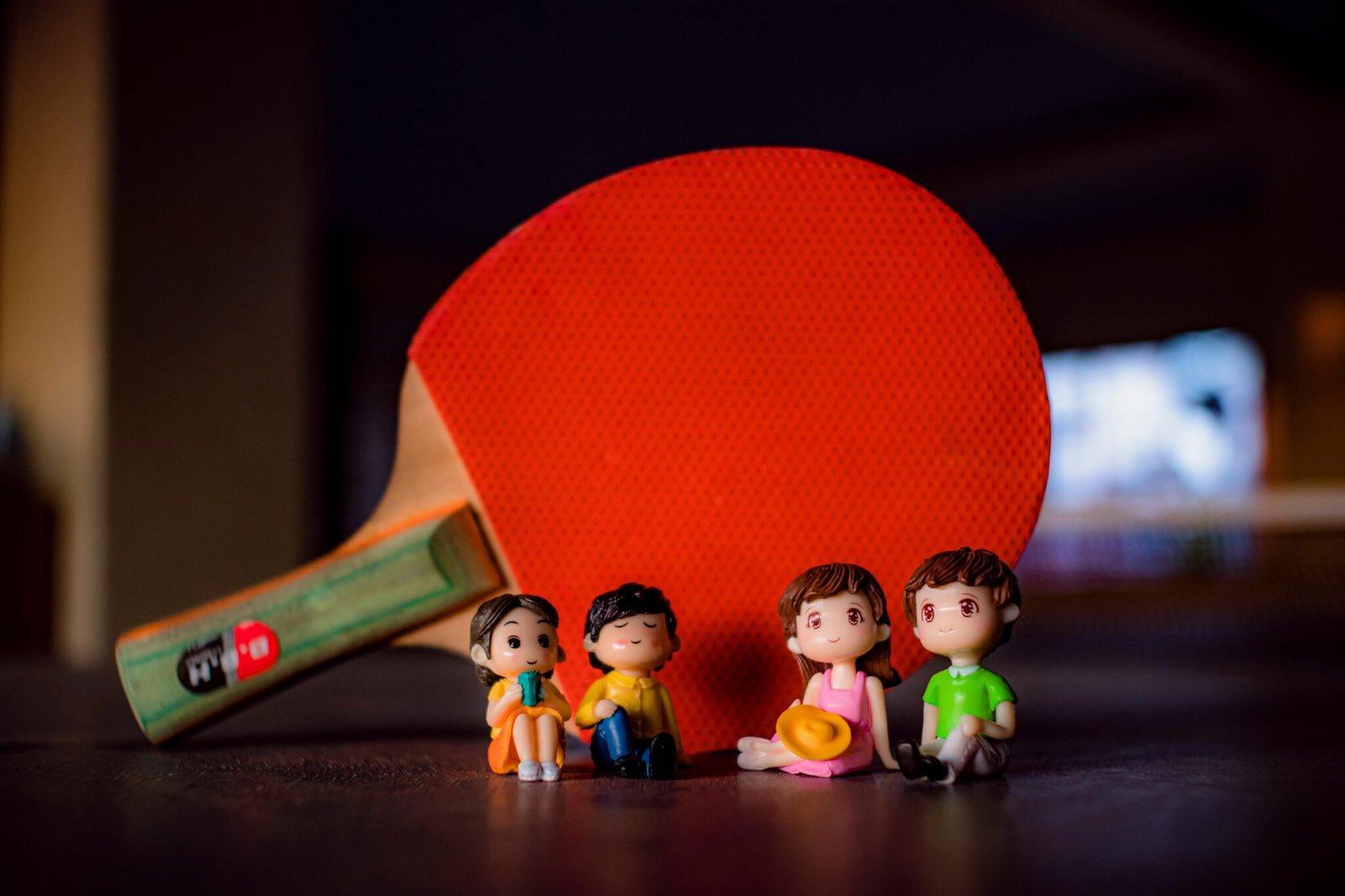 Small colorful figurines of couples placed on table near professional red table tennis racket in light room on blurred background