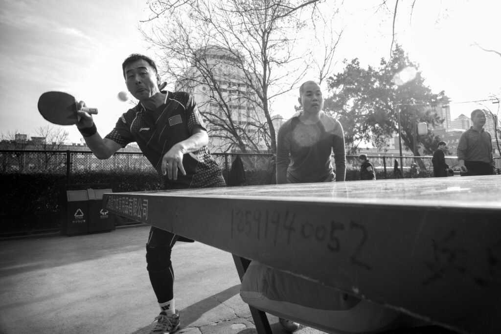Dynamic black and white photo capturing an outdoor ping pong game with two players.