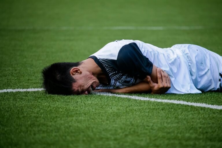 Soccer player lies on the field in pain during a game, indicating possible injury.